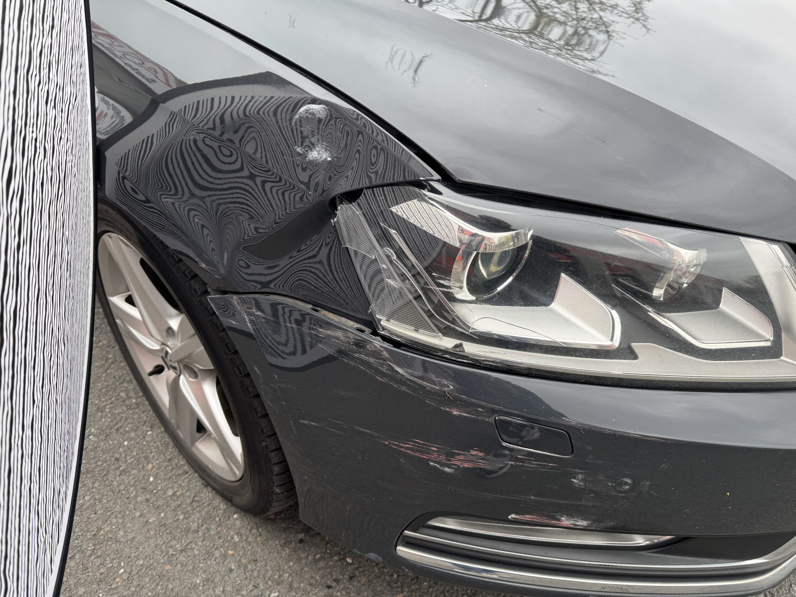 Verformter Kotflügel und Kratzspuren am vorderen Stoßfänger eines grauen Volkswagen